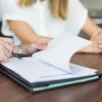 Uma pessoa aponta a outra onde ela deve assinar em um contrato